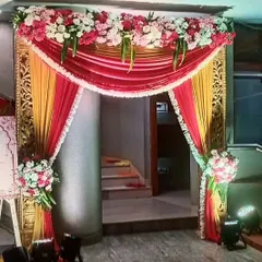 A traditional and ornate entrance arch for a wedding ceremony. The design features rich red and gold drapes, detailed side panels, and a floral border on top.