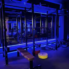 Our strength section is equipped for serious gains. This shot highlights one of our two squat racks and weight plates, all set against our signature blue ambient lighting that creates an energetic workout environment.