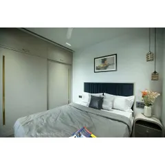 This master bedroom at Tulsi Heights uses a dark, moody theme to create a cozy and intimate atmosphere. The deep blue headboard and sleek wooden flooring contribute to the modern classic look.