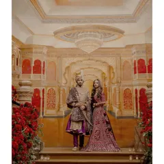 A portrait of pure royalty. The couple stands on the steps of a grand staircase in a Mumbai palace, their regal attire perfectly complementing the opulent surroundings.