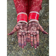 The beautiful dark stain of a Karwachauth mehndi, perfectly complemented by red bangles. This design features traditional portraits for the festival.