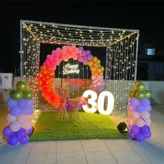 I transform terraces into stunning party spaces, like this 30th birthday celebration. The decor includes a canopy of fairy lights, a colorful balloon ring, a "Happy Birthday" neon sign, and large light-up marquee numbers.