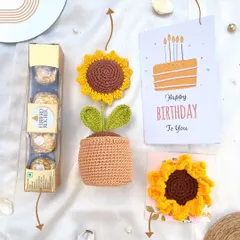 A flat-lay of our sunflower birthday hamper, showing all the contents: a box of Ferrero Rocher, a handmade potted crochet sunflower, a birthday card, and a sunflower hair clip.