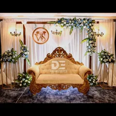 An elegant engagement stage featuring a custom monogram with the couple's initials. The design combines soft white drapery, a classic carved sofa, and asymmetrical blue and white floral arrangements for a sophisticated and personal look.