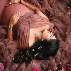 An artistic overhead shot of a mother-to-be surrounded by flowers and a sea of dusty rose tulle, creating a truly magical image.