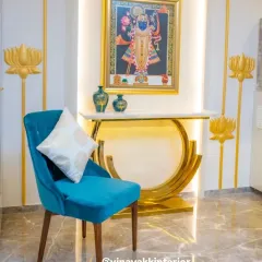 We created this vibrant spiritual corner using a statement console table with a gold base, a traditional Pichwai painting of Lord Krishna, and decorative lotus wall art. The pop of color from the velvet chair completes this elegant setup.