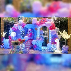 A vibrant and colorful butterfly-themed first birthday stage. This setup features a stunning mix of blue and pink balloons, illuminated butterfly props, and a light-up arch that frames the backdrop, creating a dreamy and magical atmosphere.