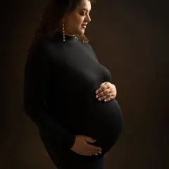 In the quiet of the studio, with just a simple black gown and soft lighting, a mother's strength becomes the entire story. This classic, minimalist maternity portrait focuses on the beautiful silhouette of pregnancy, creating a timeless piece of art.