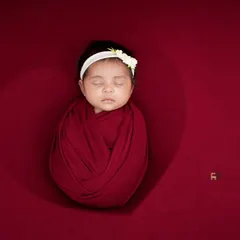 This newborn is wrapped in a rich red swaddle against a matching backdrop, creating a striking and heartfelt image. The heart-shaped lighting effect adds a touch of love to this classic potato sack pose.