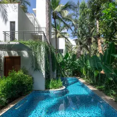 At the SANCTUM House, the swimming pool is designed as a natural element that meanders alongside the home, flanked by the lush greenery of an existing coconut grove. This design choice creates a resort-like feel and reinforces the home's connection to its landscape.