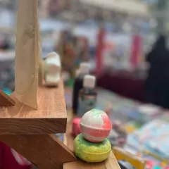 A close-up shot of my bath bombs stacked on the display shelf. The blurred background shows the busy atmosphere of the market, but these little balls of joy always stand out.