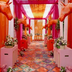 Haldi, but make it equestrian chic. This bold entranceway combines vibrant pinks and oranges with floral-adorned horse sculptures to create a whimsical and unforgettable welcome for a fun-filled celebration.