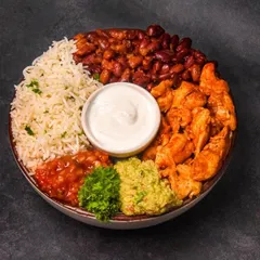 A vibrant and healthy chicken burrito bowl, neatly arranged with cilantro lime rice, seasoned chicken, kidney beans, fresh guacamole, and salsa. The top-down flatlay composition on a dark surface highlights each fresh ingredient.