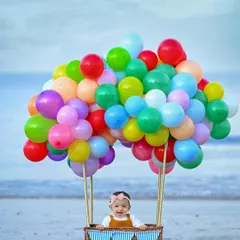A creative and whimsical baby portrait featuring a little one in a hot-air balloon basket on the beach. This themed shoot uses colorful balloons and a natural seaside setting to create a magical and unforgettable image.