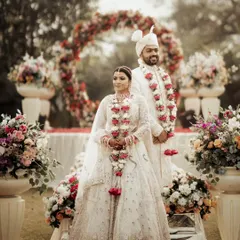 A formal portrait of the couple at their floral mandap, showcasing their coordinated white wedding attire and the beautiful decor.