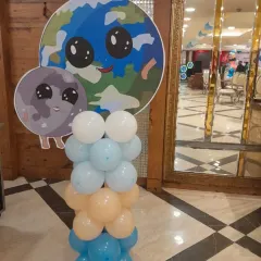 A cute space-themed balloon pillar featuring a cartoon earth and moon cutout. These standalone decorations are perfect for placing around a room to enhance the party's theme.