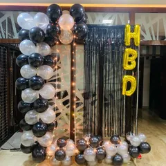A simple yet striking birthday decoration. I used black and white balloons to create a partial arch, set against a black fringe curtain with 'HBD' foil letters and a string of fairy lights for a cozy glow.