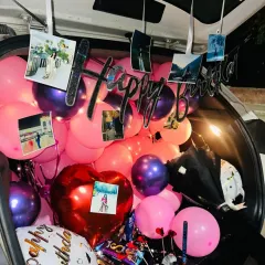An overhead view of the birthday car boot decor, showing the 'Happy Birthday' sign, photos, and a large heart-shaped balloon.