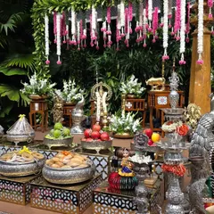 A detailed shot of the offerings, including fruits and sweets in silver bowls, set against the garden backdrop.
