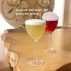 Two elegant cocktails, one with a lemon twist and the other with a vibrant red hue and foam, showcasing a bar's potent and pretty creations.