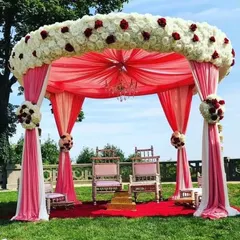 An elegant outdoor Vidhi Mandap we designed at a resort, featuring a beautiful floral canopy of white and red roses with flowing pink drapes. We create sacred and beautiful spaces for you to take your vows.
