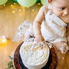 Let the mess begin! This little one is just starting to dig into his first birthday cake during his at-home cake smash session. The lit-up number '1' and simple balloon decor create a festive, personal setting.