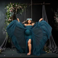 A joyful and dynamic studio portrait of a woman on a swing, her blue gown fanning out around her. The dark floral backdrop and her happy expression make this a truly captivating image.