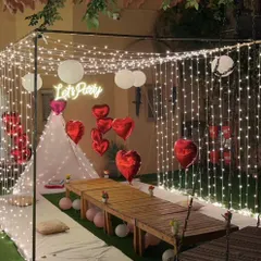 An enchanting evening party setup on a terrace. A canopy of fairy lights creates a magical ceiling over a cozy seating area with a teepee tent and heart-shaped balloons.