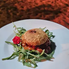 This bite-sized creation features a crispy, breaded patty served on a bed of savory relish and fresh greens. It is a perfect example of how we create complex, multi-layered flavors in a single canapé.