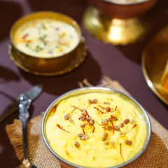 A bowl of creamy, saffron-infused Shrikhand, a traditional yogurt-based dessert. The rustic textures and deep colors evoke a sense of homemade comfort and festive indulgence.