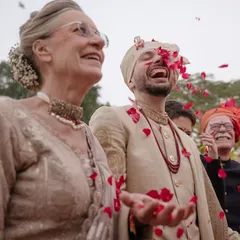 Ted shares a laugh with his mother, showered in red petals from Karna's family. This is a beautiful moment of two families coming together, filled with genuine happiness and warmth.