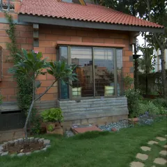 A bay window at the Sharada Residence provides a cozy interior nook while adding character to the exterior facade. The combination of brick, stone, and a tiled roof canopy reinforces the home's rustic, traditional feel.