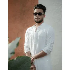 A stylish portrait of the groom against a modern, color-blocked wall, his sunglasses adding a touch of cool to his traditional outfit.