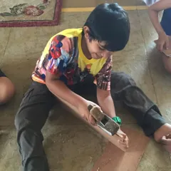 A young builder using a hand planer to shape a piece of wood. We teach basic woodworking skills, fostering a sense of accomplishment and confidence.