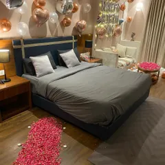 A full view of a sophisticated birthday room makeover. This angle shows the path of red rose petals on the floor, leading towards the decorated bed and a side table also covered in petals, tying the whole romantic theme together.