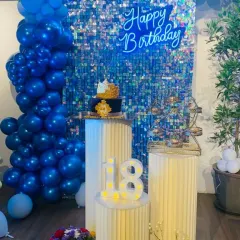 An 18th birthday celebration with a royal blue theme. The blue shimmer wall, matching balloon garland, and custom cakes create a cohesive and striking look for this important milestone.