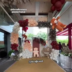 An elegant entrance for a teddy bear themed baby shower. The color scheme of maroon and peach, combined with pampas grass and a gold carpet, sets a sophisticated tone right from the start.