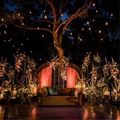 An intimate and romantic outdoor seating area designed for a cocktail evening. We used the natural beauty of a large tree as a centerpiece, draping it with Edison bulbs to create a warm, inviting glow over the floral-adorned stage.