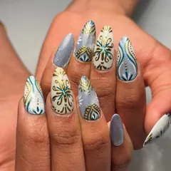 A full look at these custom Navratri press-on nails. The design features intricate gold and teal patterns on a mix of white and glittery blue almond-shaped nails, perfect for getting into the garba spirit.