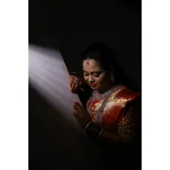 An artistic shot of the bride's reception look. The dramatic lighting highlights her flawless makeup and the rich details of her red and gold saree.