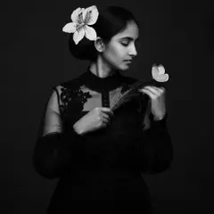 This introspective portrait in black and white feels even more poetic. The absence of color draws attention to the delicate forms of the flower, feather, and her expression.