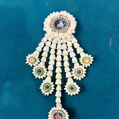 A custom floral hair brooch featuring a small image of a deity at the center. The piece is made from jasmine buds and decorated with small flowers and stones.