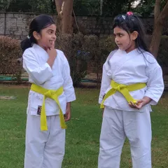 Two students, who have earned their yellow belts, share a secret during a break in our park class. Our outdoor sessions are a great place for kids to practice and strengthen their friendships.
