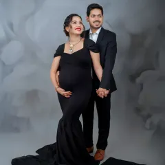 A sophisticated studio portrait of the couple. Their formal black attire against the textured grey backdrop creates a very chic and modern look.