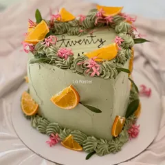 A unique heart-shaped cake in a lovely sage green color. I decorated it with fresh orange slices and tiny pink flowers for a vibrant, modern, and natural look.