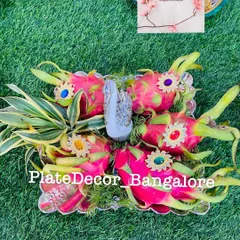 A platter of vibrant dragon fruits, each adorned with a colorful kundan stone. The arrangement is completed with a silver swan figurine and fresh leaves.