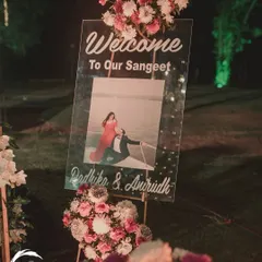 A personalized welcome to the Sangeet. This clear acrylic sign features the couple's pre-wedding photo, creating a warm and personal greeting for their guests.