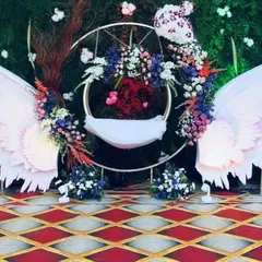 I design unique and modern cradle setups for naming ceremonies. This angel-wing themed 'thottilu' creates a heavenly centerpiece for your baby's special day, combining artistic cutouts with lush floral arrangements.