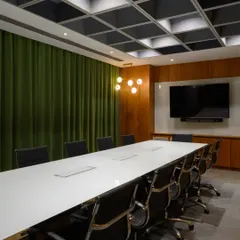 This meeting room proves that corporate spaces can have color. The rich green acoustic curtains not only help with sound but also add a bold, sophisticated touch against the warm wood paneling and modern grid ceiling.