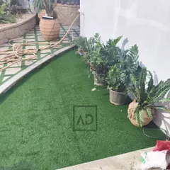 This project involved laying artificial grass in a curved garden space next to existing potted plants. The result is a consistently green lawn area that complements the real plants and is easy to keep clean.